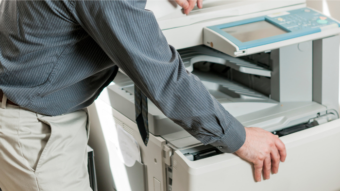 A man opens his office photocopy machine to repair a paper jam.