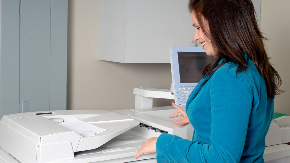 A woman stands at a printer and is having a good day copying documents.