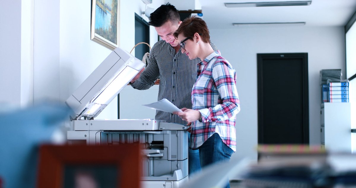 A man and woman working on a large office printer. Office printer rental allows business owners to save money while maintaining high quality technology.